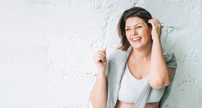 Beautiful happy brunette young woman plus size body positive in comfortable sport wear near white brick wall, banner