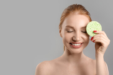 Fototapeta na wymiar Happy woman with makeup sponge on grey background