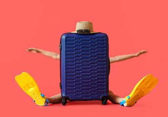 Funny little boy in paddles sitting behind suitcase on color background