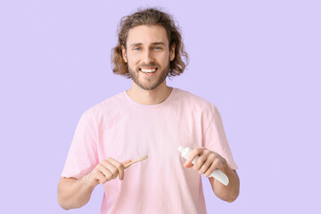 Handsome young man with tooth brush and paste on lilac background