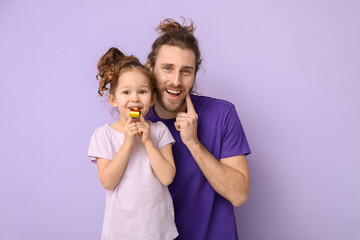 Funny man and her little daughter with party blower on lilac background. April fools' day celebration