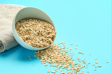 Bowl with raw oatmeal flakes on blue background