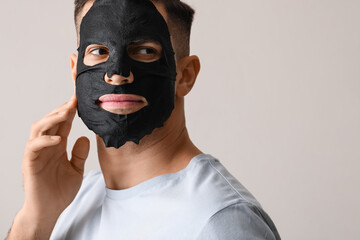 Handsome man with black facial mask on grey background, closeup
