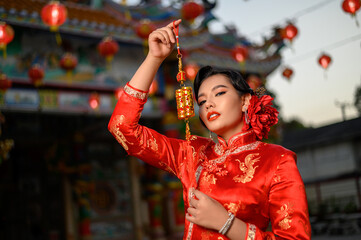 Asian beautiful woman wearing a cheongsam poses with china auspicious amulet at shrine