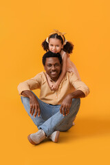Portrait of little African-American girl and her father on yellow background