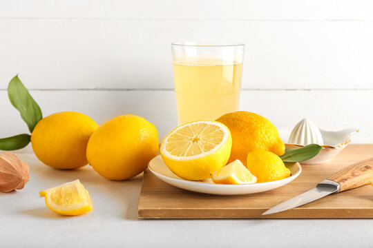 Wooden board with ripe lemons and glass of juice on light table