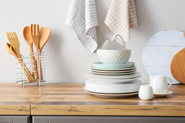 Beautiful dinnerware and kitchen utensils on counter near light wall - obrazy, fototapety, plakaty