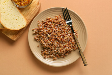 Plate of tasty buckwheat porridge and bread on color background