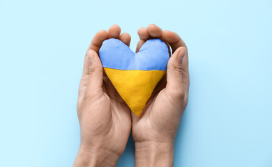 Hands holding heart in colors of Ukrainian flag on blue background