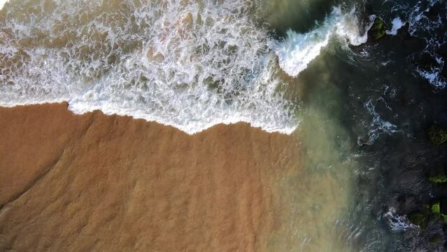 waves breaking at black rocks in Geriba Beach in Buzios, Brazil, Aerial top down view