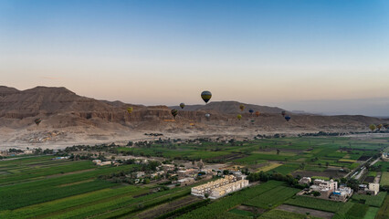Fototapeta na wymiar Balloons are flying over the Nile Valley. Below you can see green plantations, village houses. A mountain range against the background of the morning sky. Egypt. Luxor