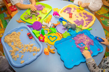 Childrens of European appearance playing with lilac kinetic sand and animals figure