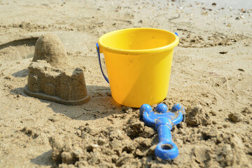 Fototapeta na wymiar Close-up sand castle on the beach with yellow plastic basket kids toys and blue rake kids toy.