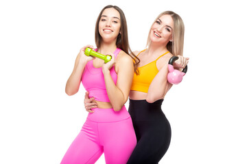 Two beautiful, athletic, slender and cheerful female friends are smiling and holding dumbbells and a kettlebell in their hands. Lifestyle concept with sports and gym. Isolated on white background.