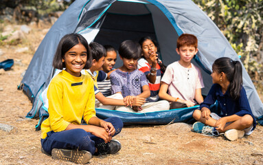 girl kid looking at camera while talking with friends at cmaping tent during summer vacation - concept of happines, outdoor activities, bonding and friendship.