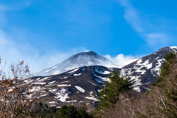 Panoramic view on north eastern flank of volcano mount Etna, in Sicily, Italy, Europe. Summit is covered with snow. Landscape is black brown volcanic sand, bare terrain. Smoke is around the craters
