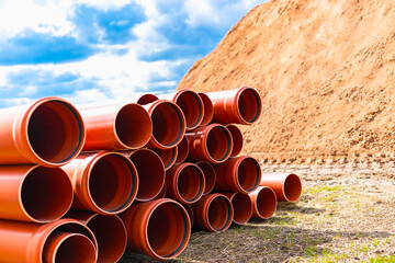 Orange sewer pipes at the construction site against the background of sand and blue sky....