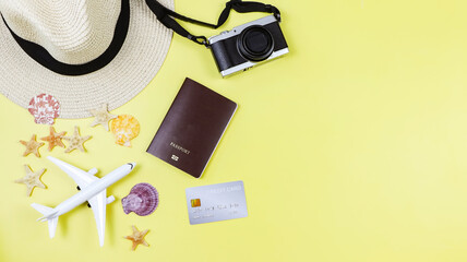  flat lay of passport, credit card, camera, straw hat, airplane model with sea shells and starfish on yellow background with copy space. Summer beach vacation background.