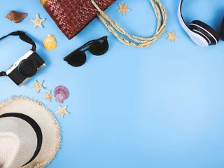 Foto auf Leinwand Top view or flat lay of  woven or rattan bag, camera, straw hat, sunglasses and headphones  on blue background, decorated with sea shells and starfishes, copy space. Summer beach vacation background. © Phuttharak
