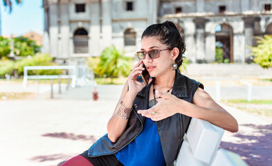 Urban style girl sitting on a bench calling on the phone, An attractive girl sitting talking on the cell phone, Girl sitting in a park calling on the phone