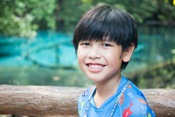 Close-up of a happy smiling boy in the background of a blue pond in a natural forest.
