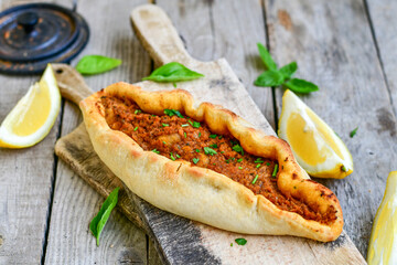  Traditional Turkish cuisine. Baked Pide dish with minced  beef, tomatoes and  herbs on  wooden background.  Turkish pizza pide