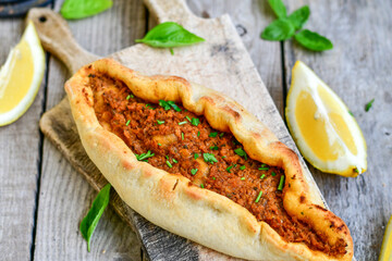  Traditional Turkish cuisine. Baked Pide dish with minced  beef, tomatoes and  herbs on  wooden background.  Turkish pizza pide