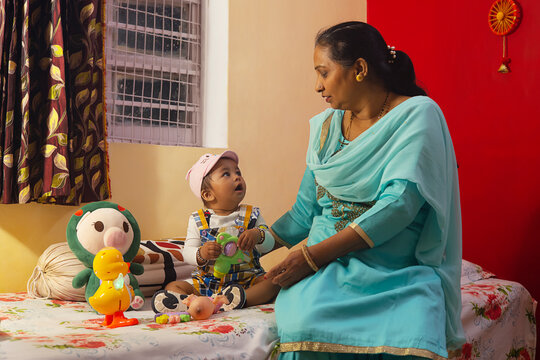 Portrait of little child and grandmother playing together with toys on bed