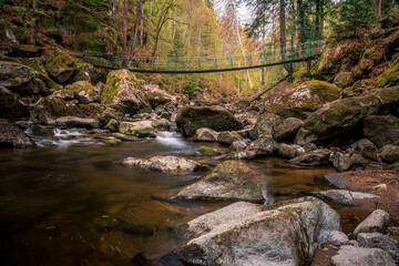 Naklejka na ściany i meble Moss stones in the river with suspension bridge in a mountain valley and green forest. Natural landscape torrent Buchberger Leite in the Bavarian Forest, Germany.
