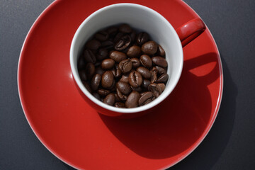 Coffee beans in a red espresso cup seen from above on a shiny grey background