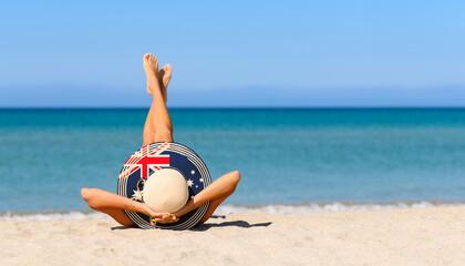 Fototapeta na wymiar A slender girl on the beach in a straw hat in the colors of the Australia flag. The concept of a perfect vacation in a resort in the Australia. Focus on the hat.