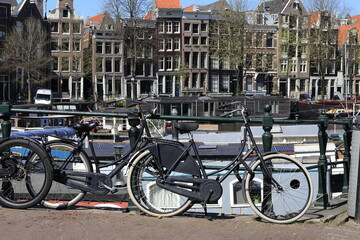 Fototapeta premium Amsterdam Kromme Waal View with Historic House Facades, Parked Bicycles on a Bridge and Houseboats, Netherlands
