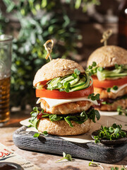 Two delicious homemade burgers with beer on wooden board at greenery background.