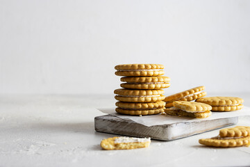 Crispy cookies with cream filling are stacked on white parchment. Wooden plank on a light table. White background, text space