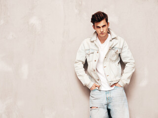 Obraz premium Portrait of handsome confident stylish hipster lambersexual model.Man dressed in jacket and jeans. Fashion male posing in studio near grey wall