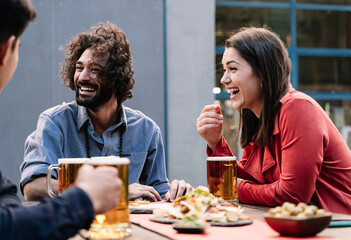 Happy friends enjoying conversation with beer and food in outdoors bar brewery, sharing good moments