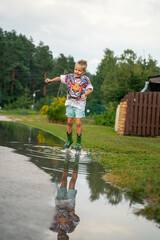 A cheerful child runs through the puddles after the rain on a warm day