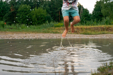 A cheerful child runs through the puddles after the rain on a warm day