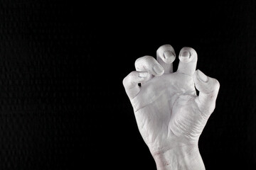 A woman's hand with contracted fingers. The gesture, the body, the tension. The hand has been painted white. A black color in the background.