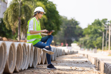 Woman construction site engineer architect worker with hard hat using tablet for checking concret...