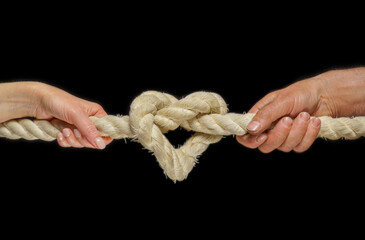  Image of a heart in the form of a rope knot. Male and female hands hold on to a thick rope. Knot...