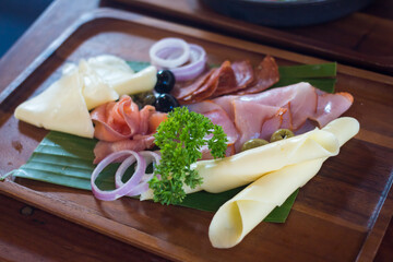 Marble cutting board with prosciutto, bacon, salami and sausages on wooden background. Meat platter