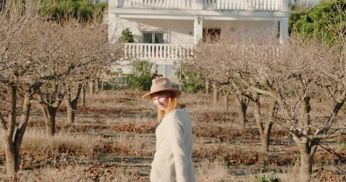 Woman walks between bare trees towards big two-storey house