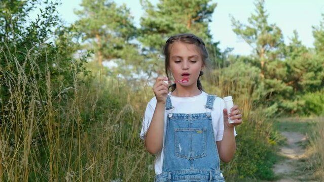 Little girl blowing soap bubbles in a city park. Child plays with soap bubbles of nature.