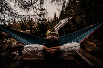 Back view of man silhouette relaxing on blue hammock between trees enjoying the view and the silent in the mountains landscape. Misty forest.