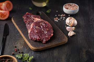 Raw fresh meat Ribeye Steak, seasoning and fresh tomato on wooden background