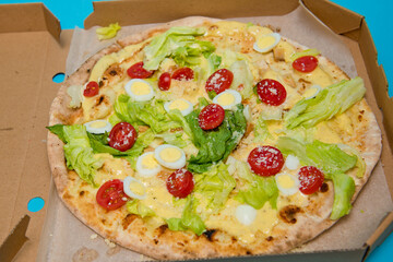 Close up of delicious hot pizza in cardboard box on light blue background. Selective focus.