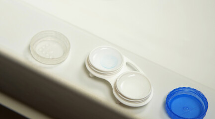 Close-up of an open container of contact lenses on a white bathroom sink. Vision problems.