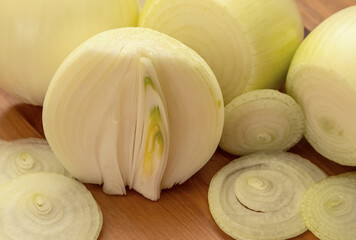 Close-up of peeled white large bulbs, one of them is cut in half and decorated with onion slices on a wooden background