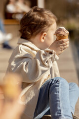 Little adorable boy sitting outdoors and eating ice cream. Lake, water and sunny weather. Child and sweets, sugar. Kid enjoy a delicious dessert. Preschool child with casual clothing. Positive emotion